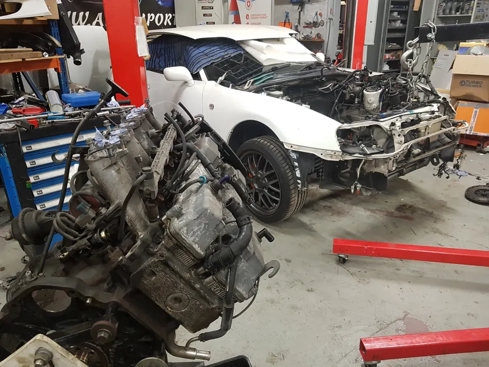 Losse motor naast witte auto met gedemonteerde neus
