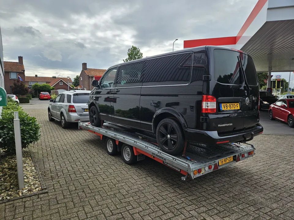 Zwarte bestelbus op trailer achter trekauto