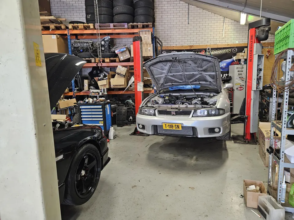 Zilveren Nissan Skyline R33 met open motorkap op brug