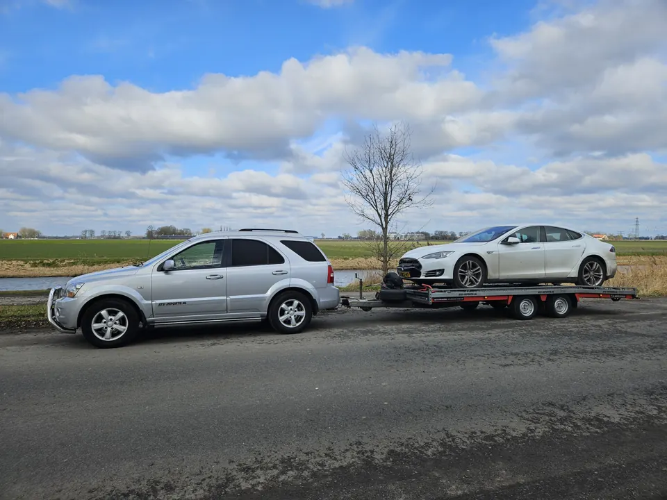 Trekauto met witte coupé op trailer in landschap