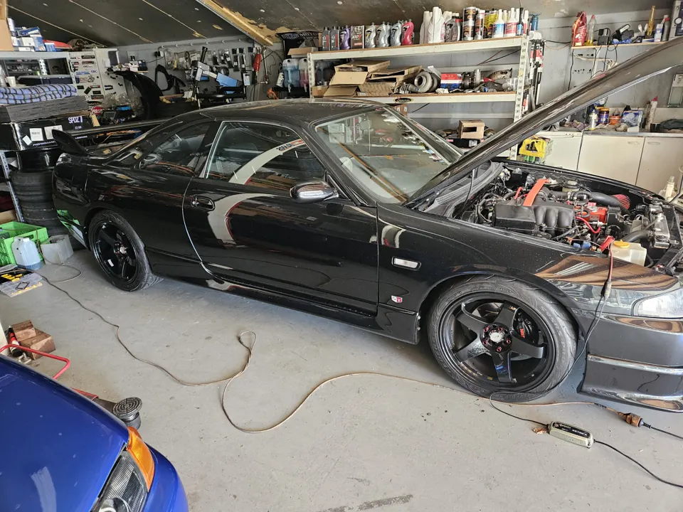 Zwarte Nissan Skyline R33 met open motorkap in werkplaats