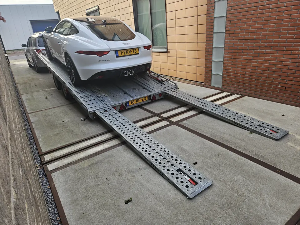 Witte sportcoupé op trailer met oprijplaten